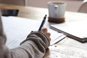 u335-Person_writing_on_brown_wooden_table_near_white_ceramic_mug