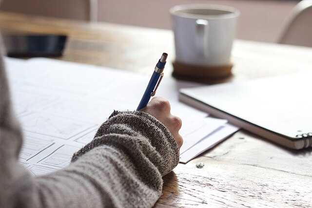 u335-Person_writing_on_brown_wooden_table_near_white_ceramic_mug